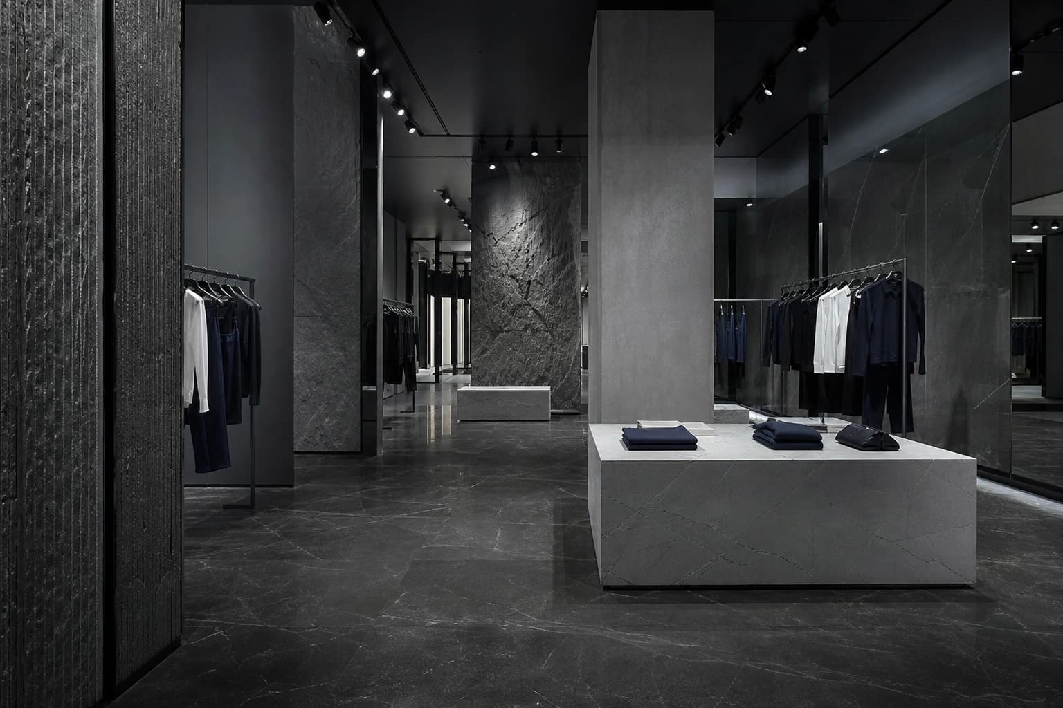 A fashion flagship interior with a polished dark stone-look floor and stone display plinths.